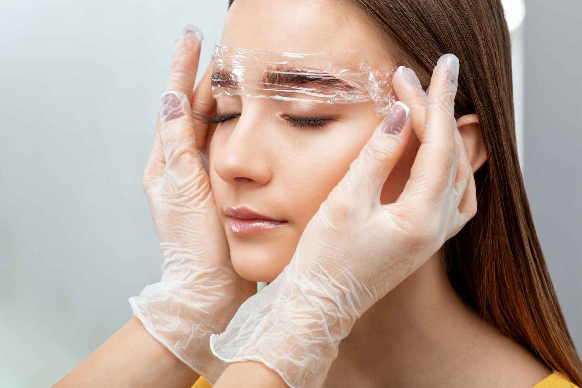 A Woman Wearing Gloves And Plastic Wrap On Her Eyebrows – Terrigal, NSW - Anjule Beauty Therapy