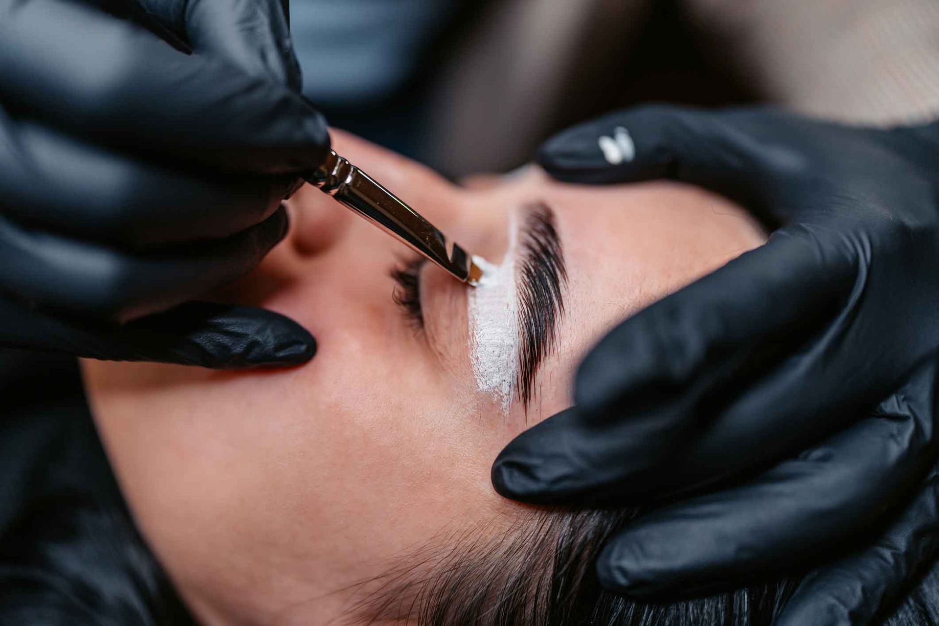 A Woman Is Getting Her Eyebrows Done By A Person Wearing Black Gloves – Terrigal, NSW - Anjule Beauty Therapy