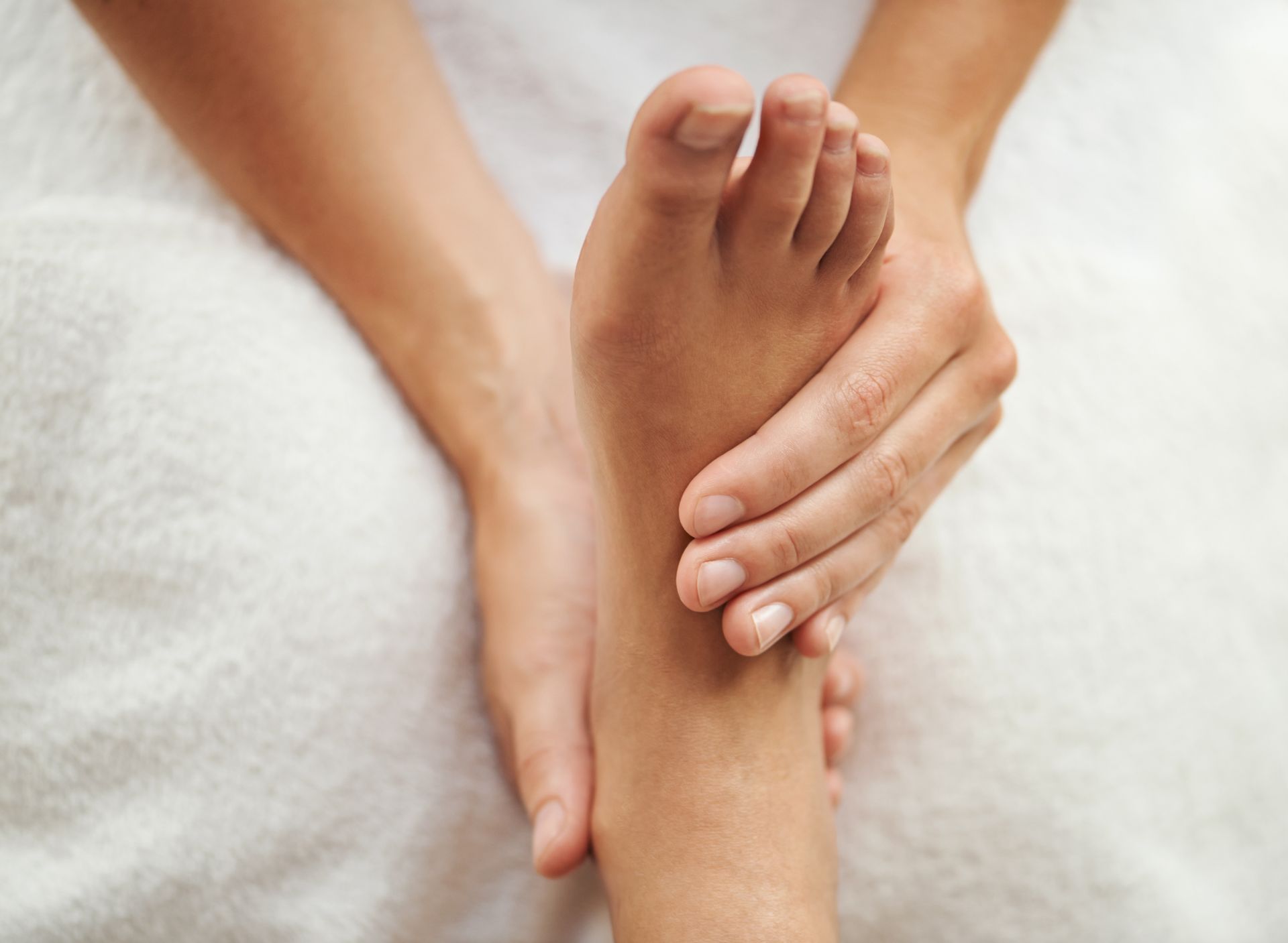 A Woman Is Holding Her Foot While Sitting On A Bed – Terrigal, NSW - Anjule Beauty Therapy