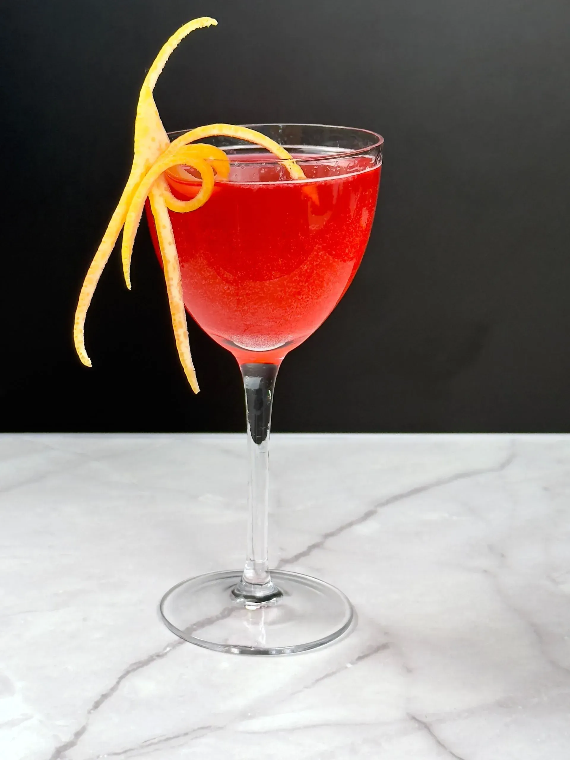 A glass of red liquid with an orange peel on top