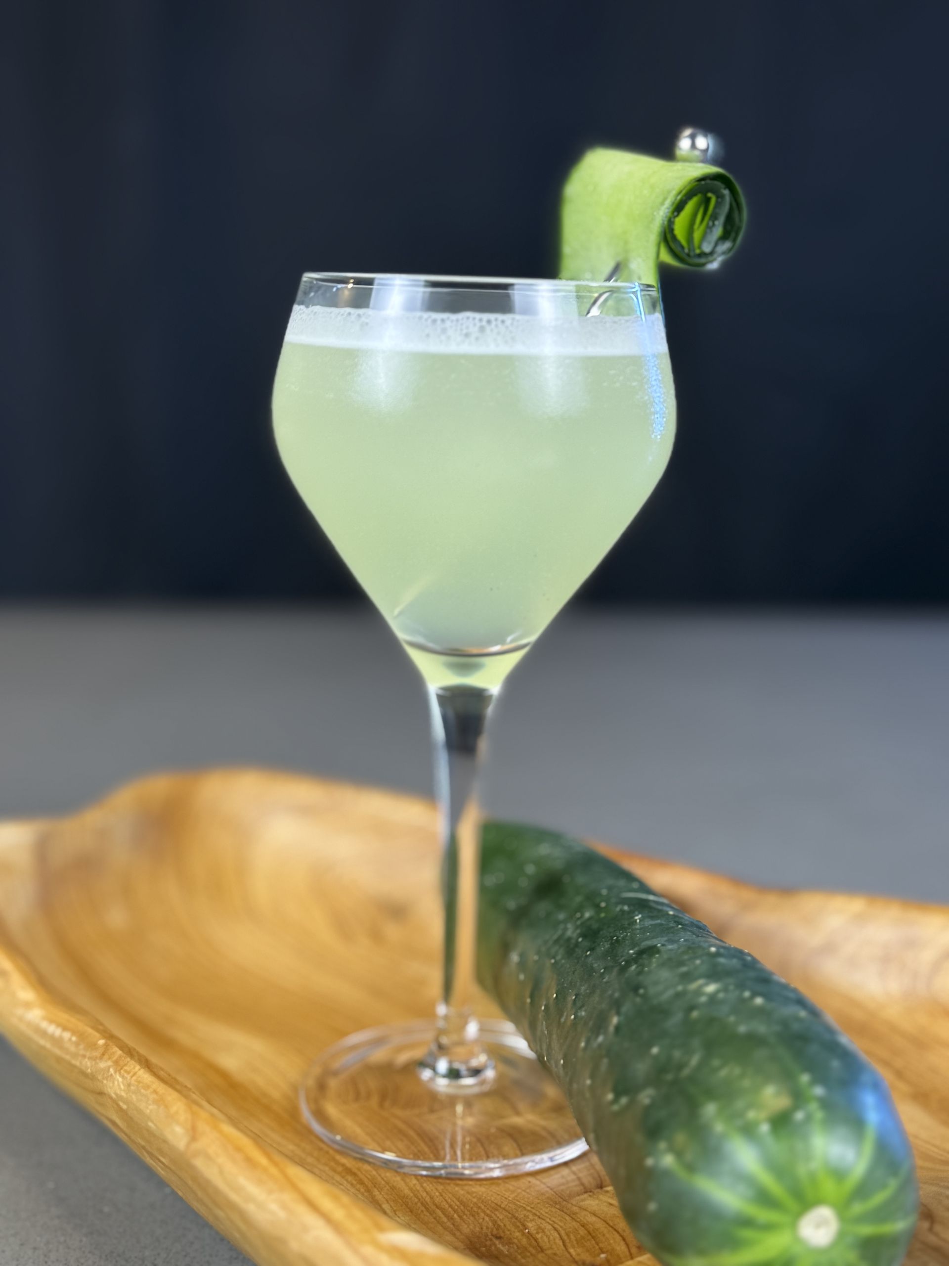 A close up of a cocktail in a wine glass next to a cucumber.