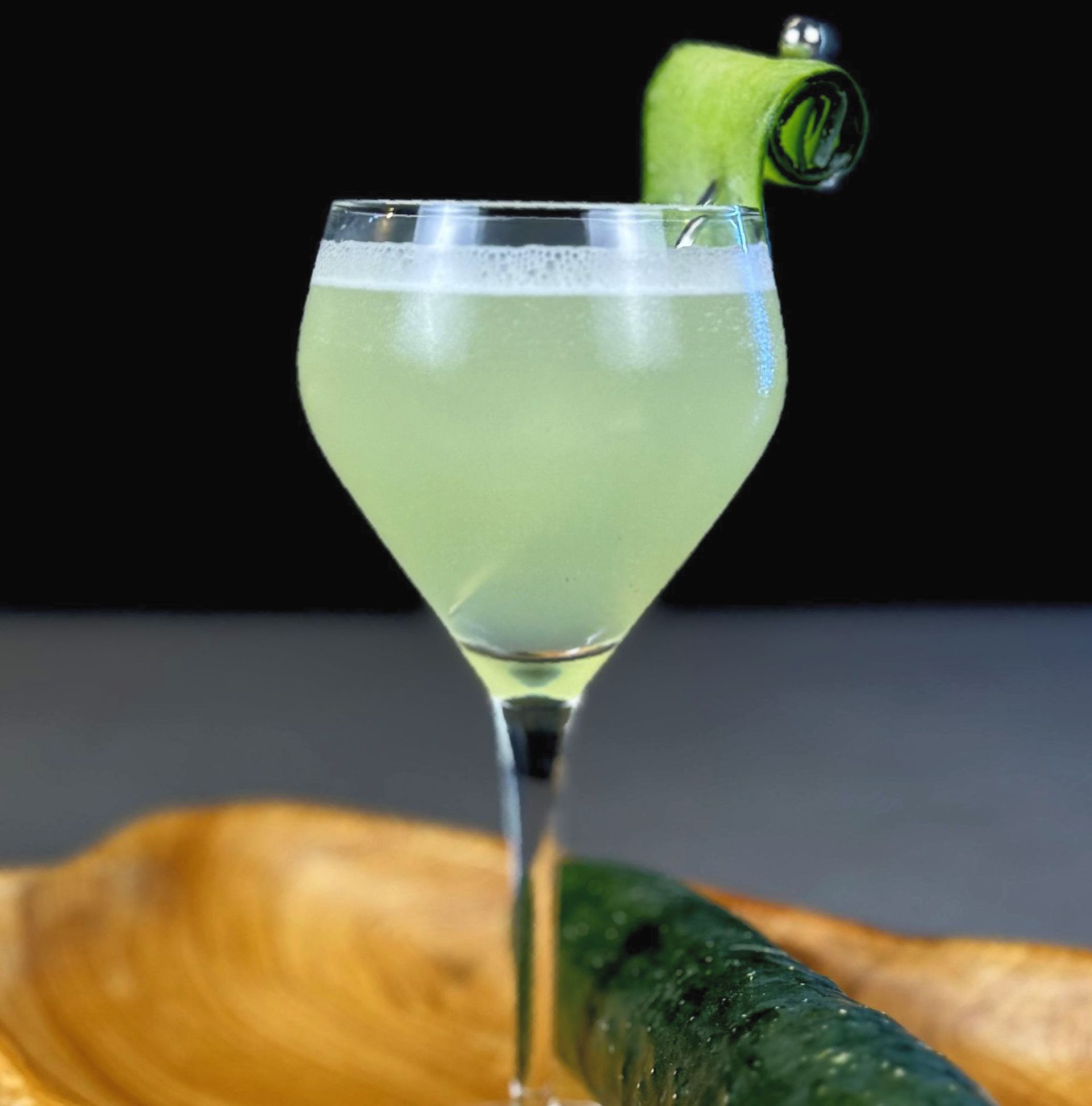 A drink in a wine glass with a cucumber garnish