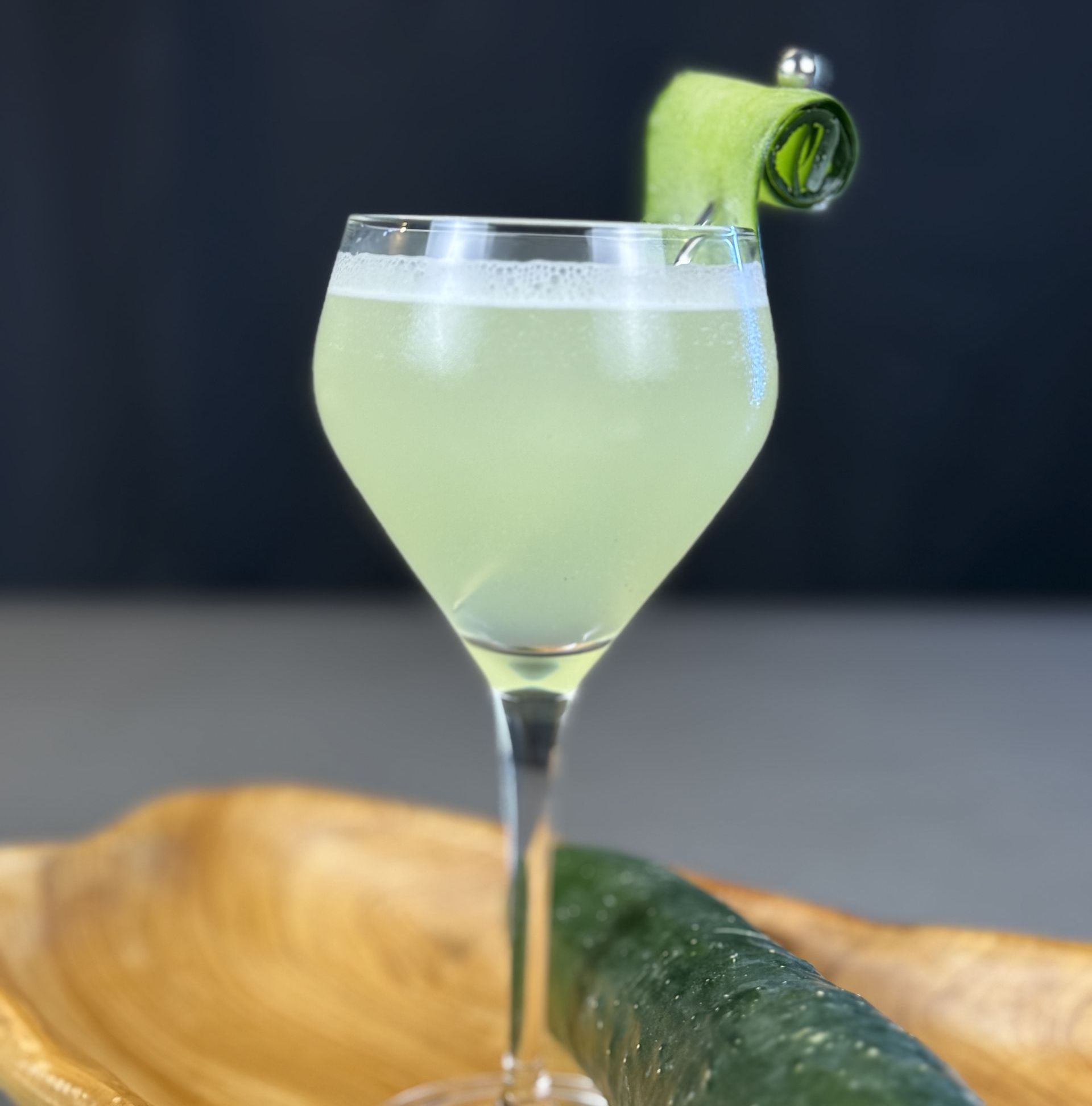 A drink in a wine glass with a cucumber garnish