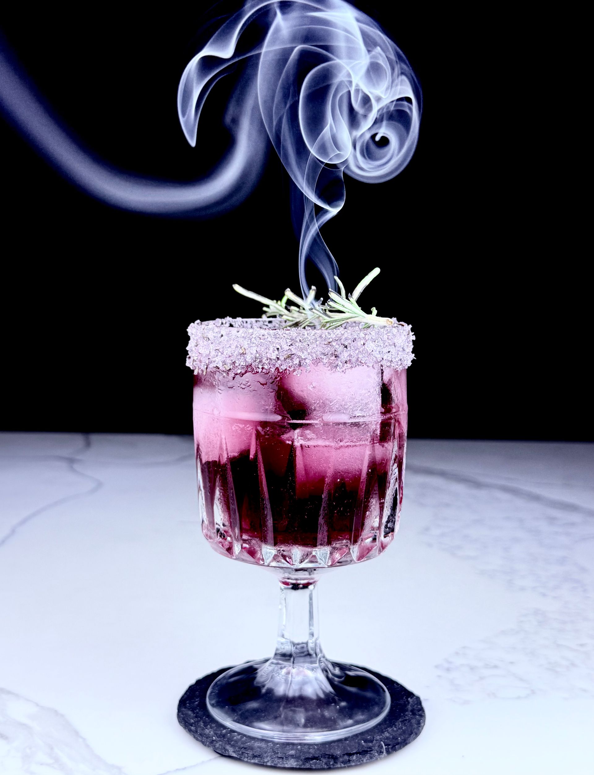 a beautiful red wine margarita with lit rosemary smoking in the center. 