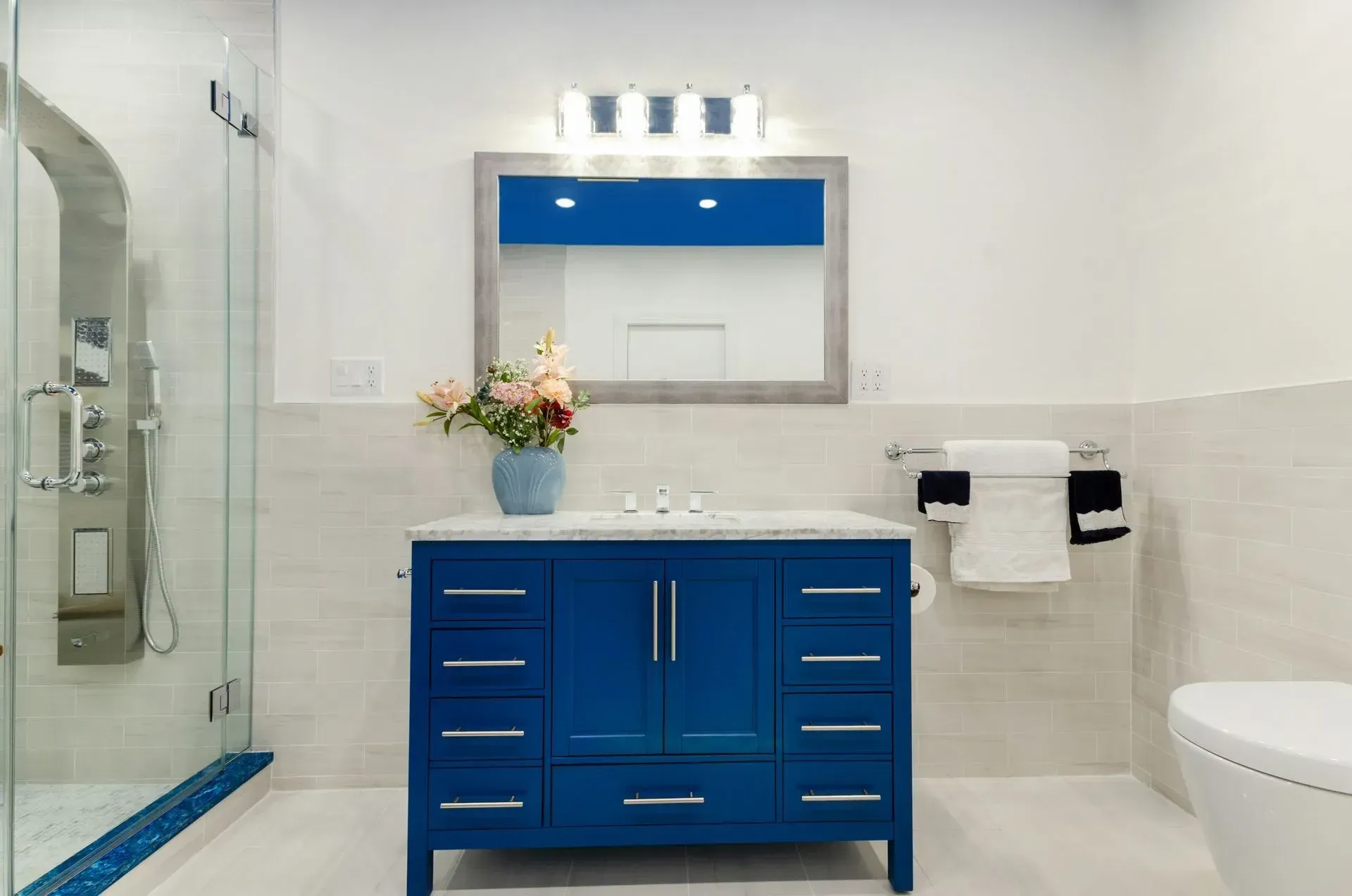 A bathroom with a blue vanity , mirror and toilet.