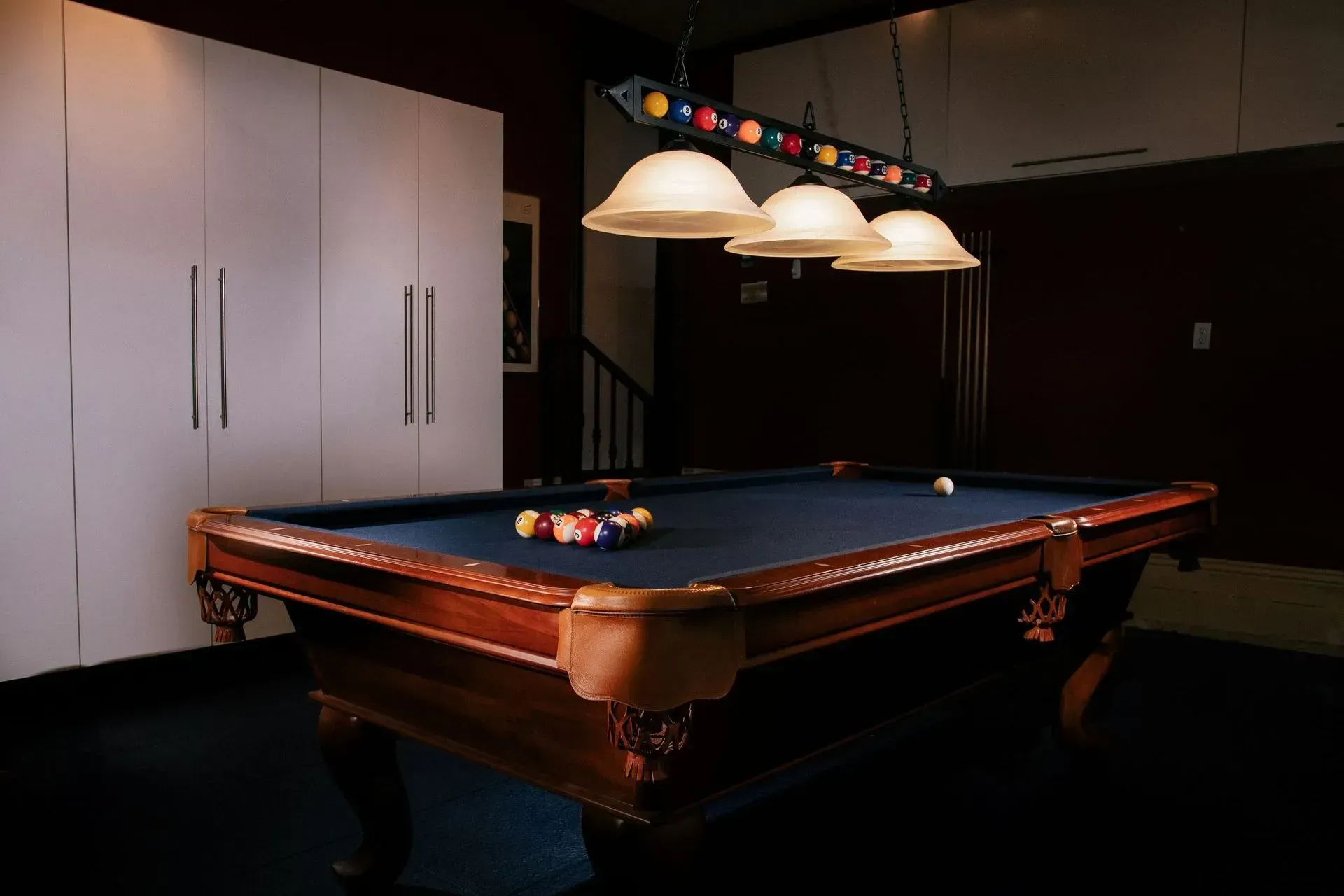 A pool table in a dark room with three lights hanging from the ceiling