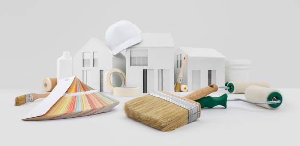 There is a model of a house and paint brushes and rollers on the table.