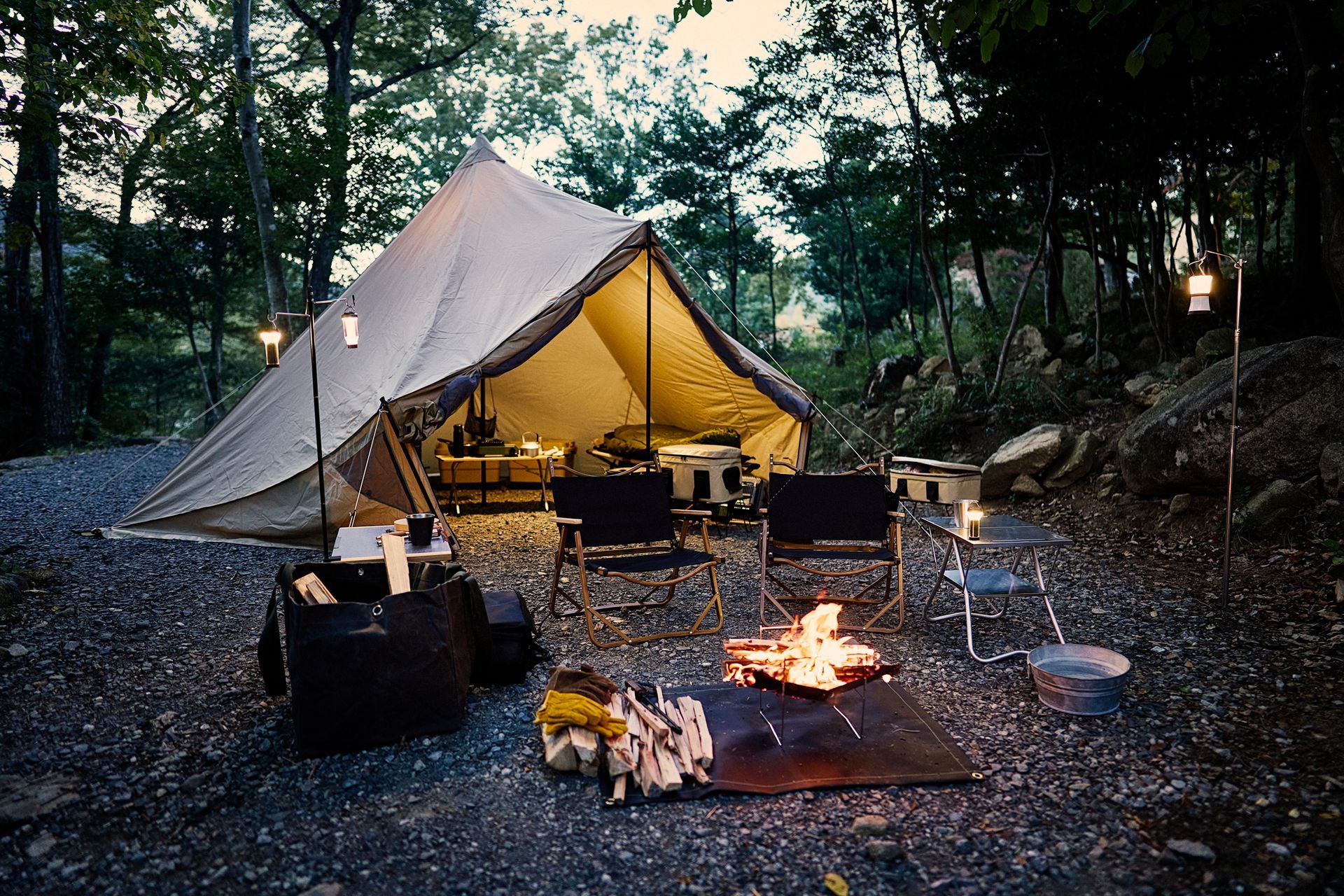 A tent is set up in the woods next to a fire pit.