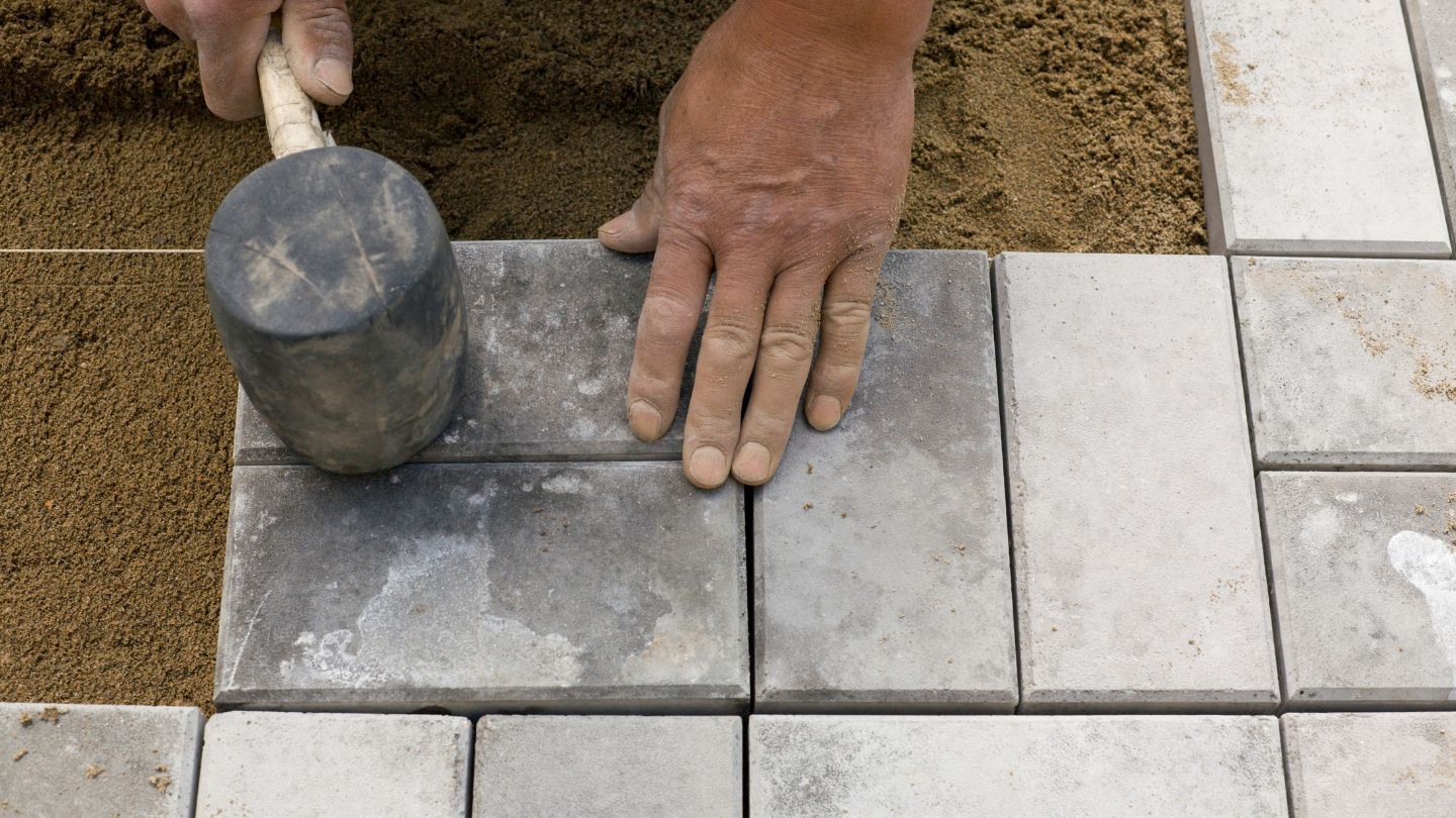 A small hammer hitting down blocks on sand for a driveway installation.