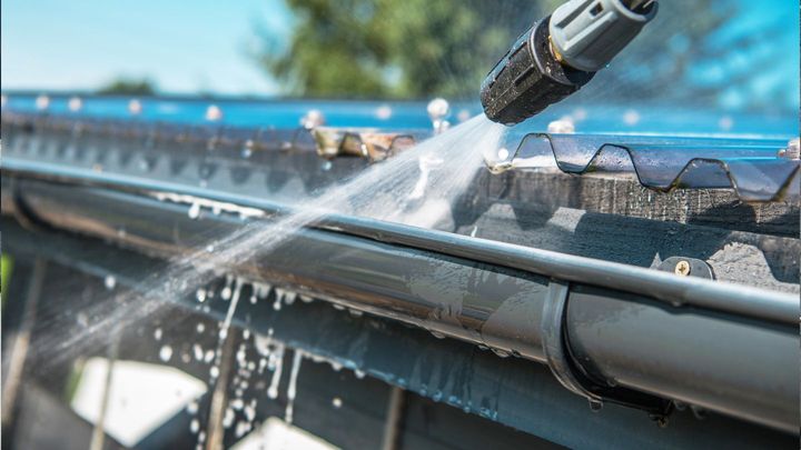A person is cleaning a gutter with a high pressure washer.