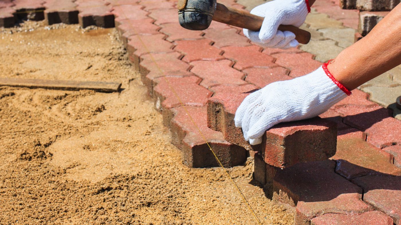 Block paving driveway installation in Exmouth, a small hammer is being used to install the red blocks on the sand. There is also a string being used to keep the installation level.