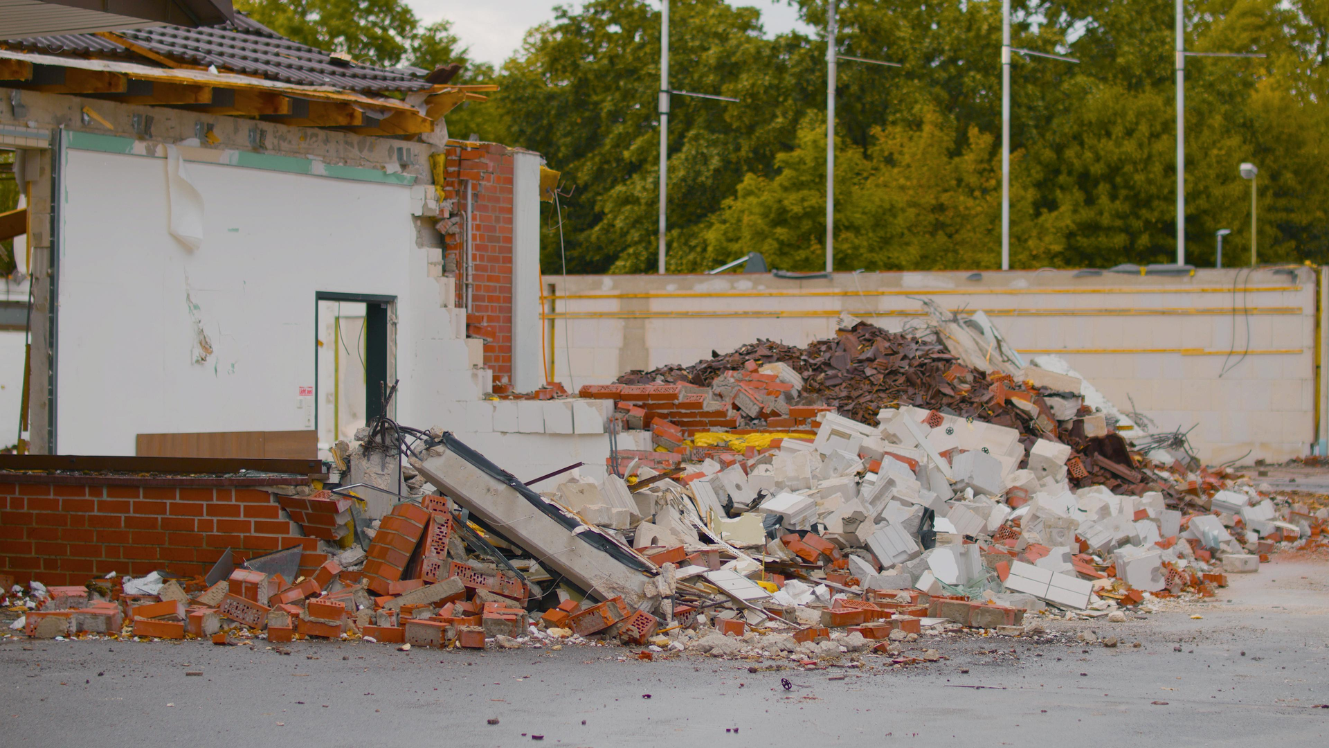A building in the process of demolition with a large pile of brick and concrete debris in the foreground.