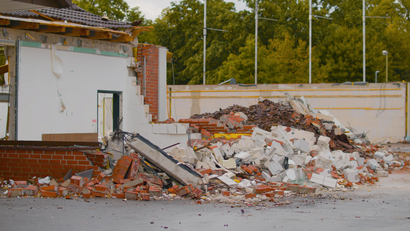 A building in the process of demolition with a large pile of brick and concrete debris in the foreground.