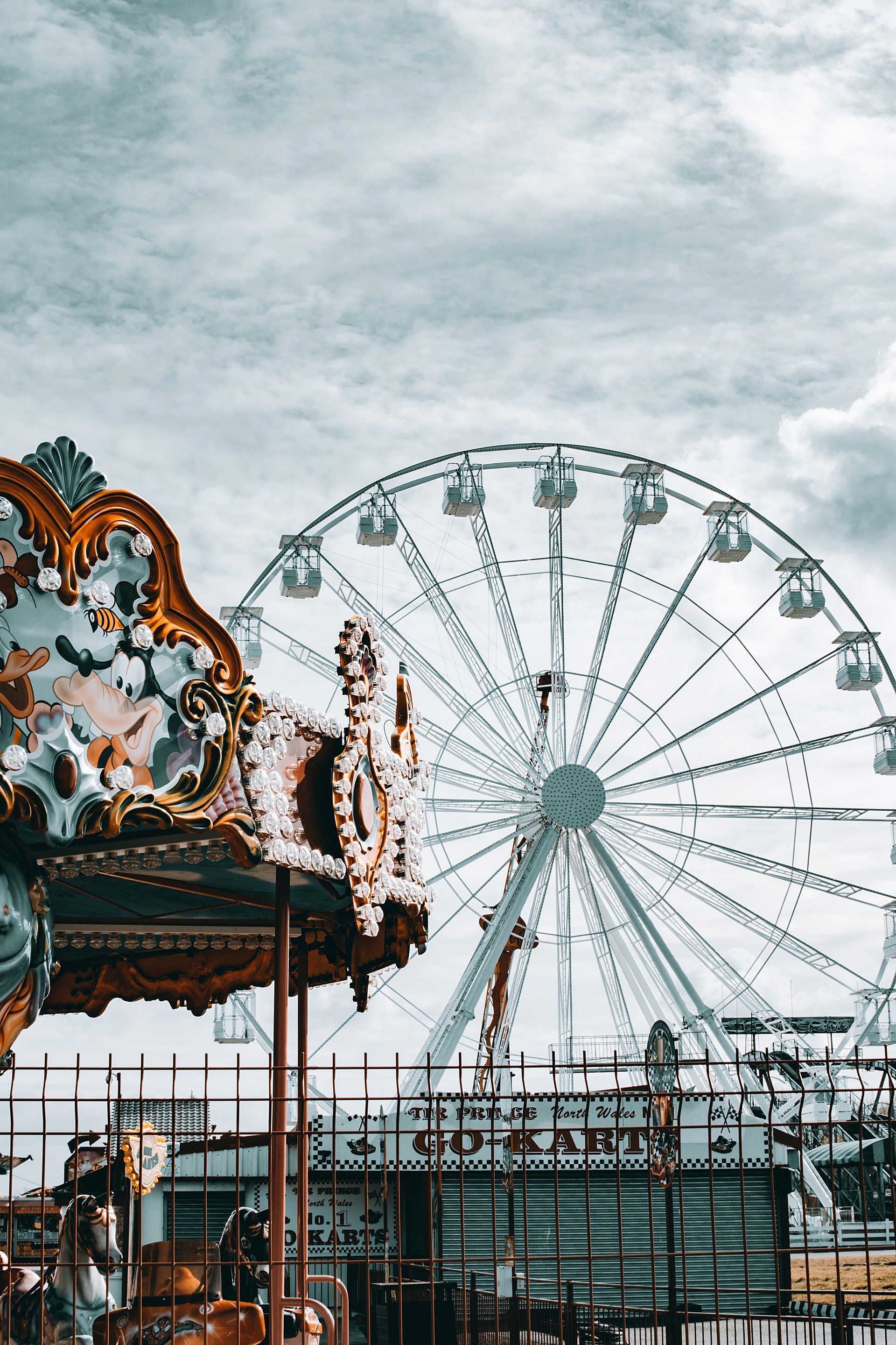 Ferris wheel and carousel against cloudy sky at amusement park.