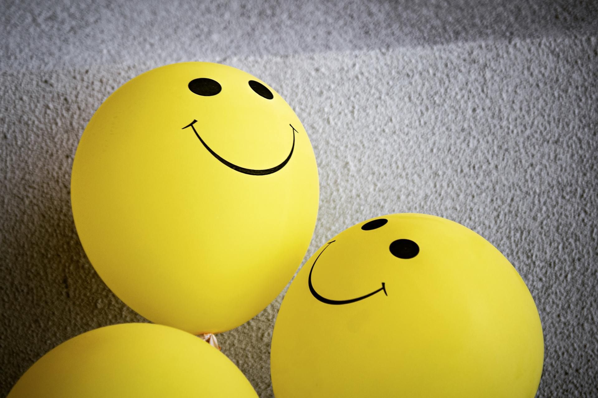 Yellow smiley face balloons against a gray textured background.