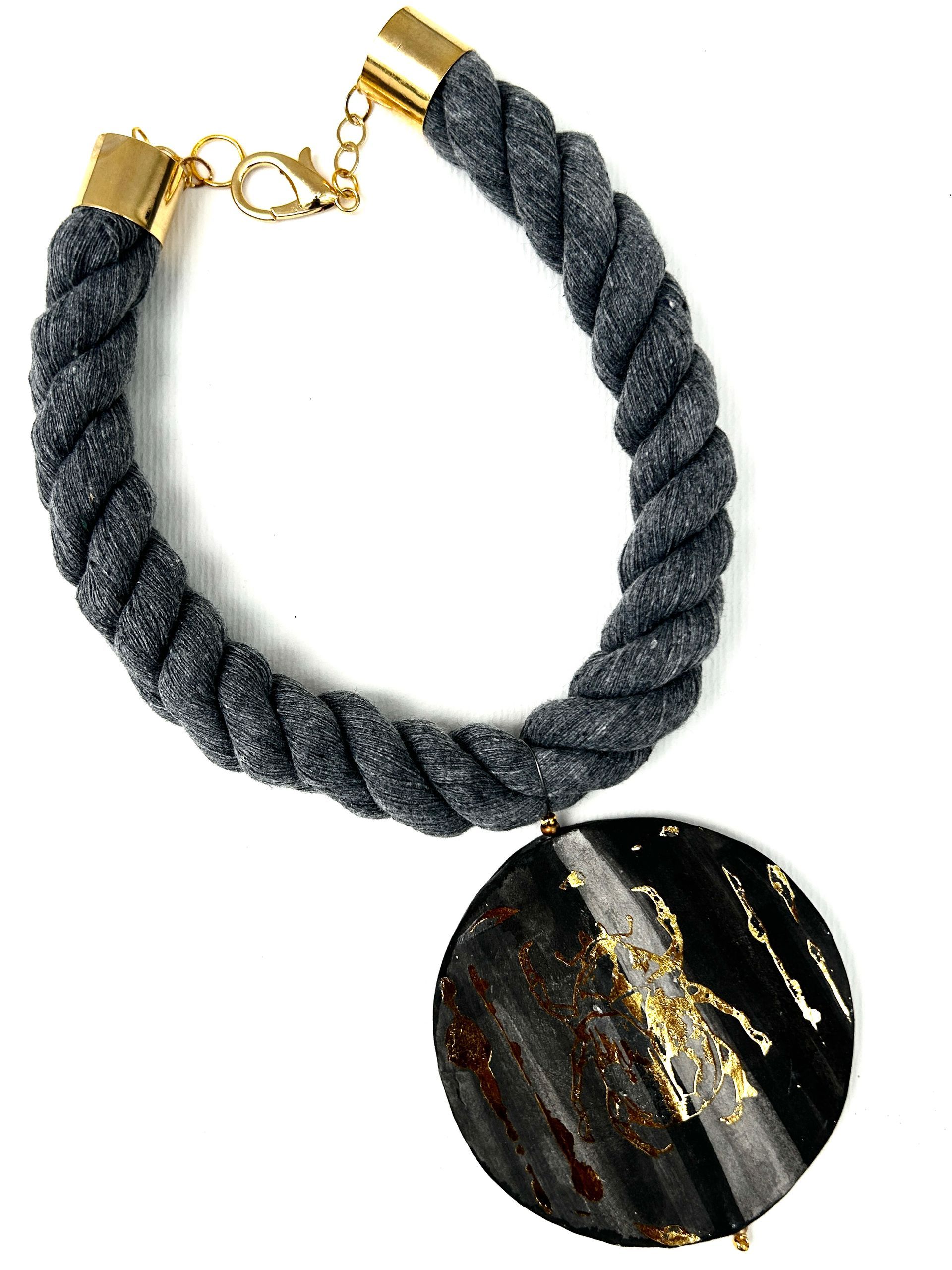 Un collar de cuerda con un colgante negro y dorado.