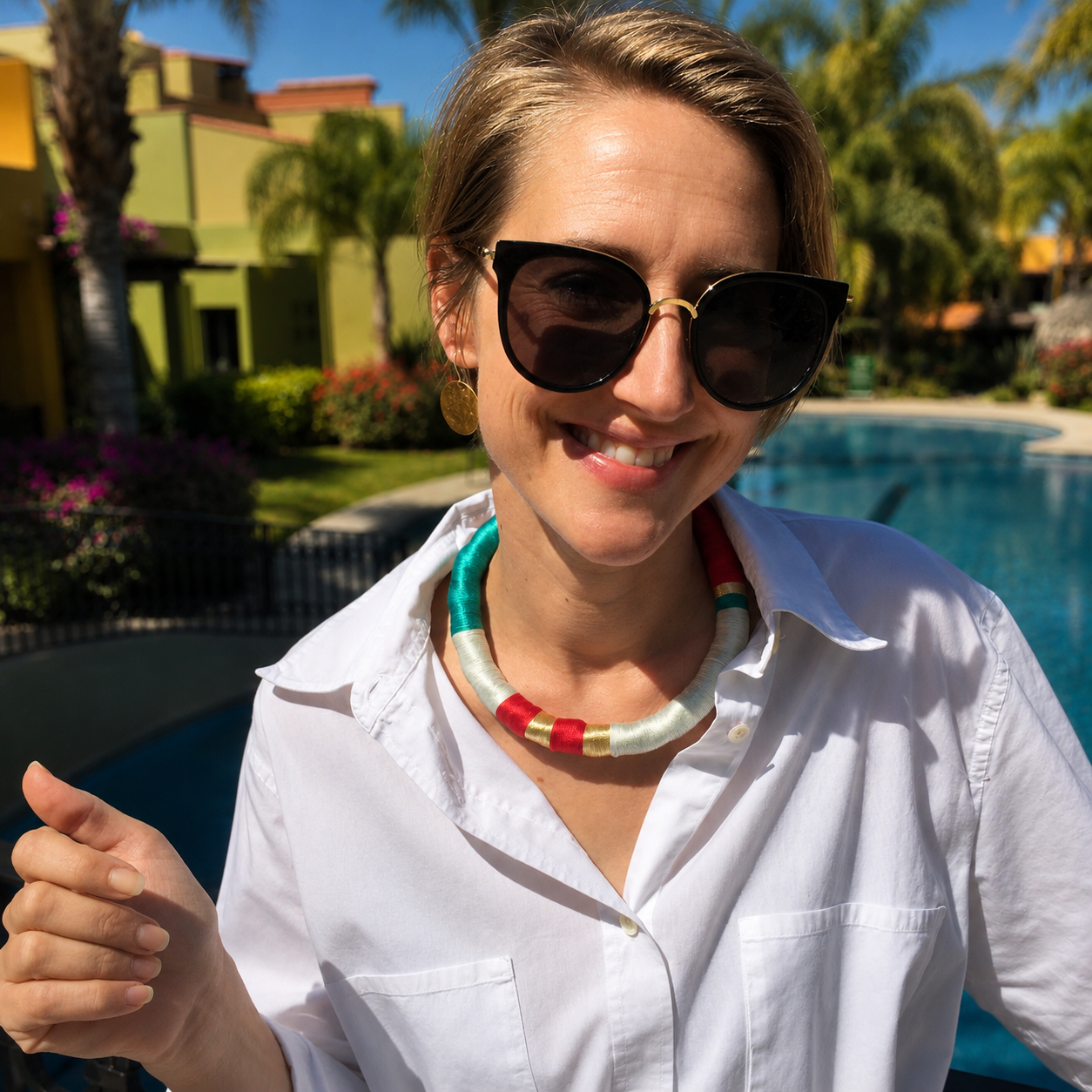 Una mujer con gafas de sol y un collar sonrรญe frente a una piscina.