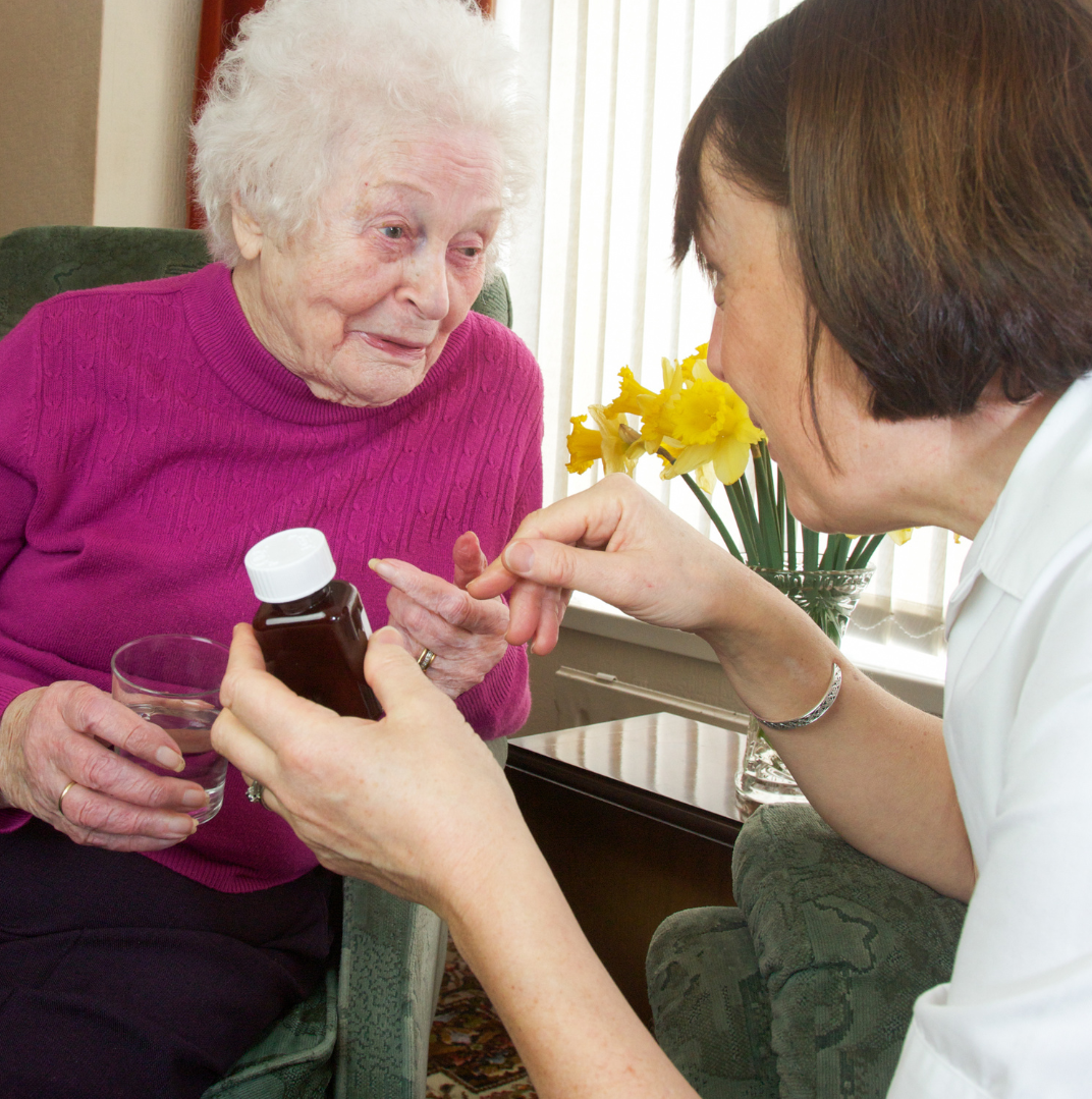 Woman giving medication to an elderly woman in a home setting.