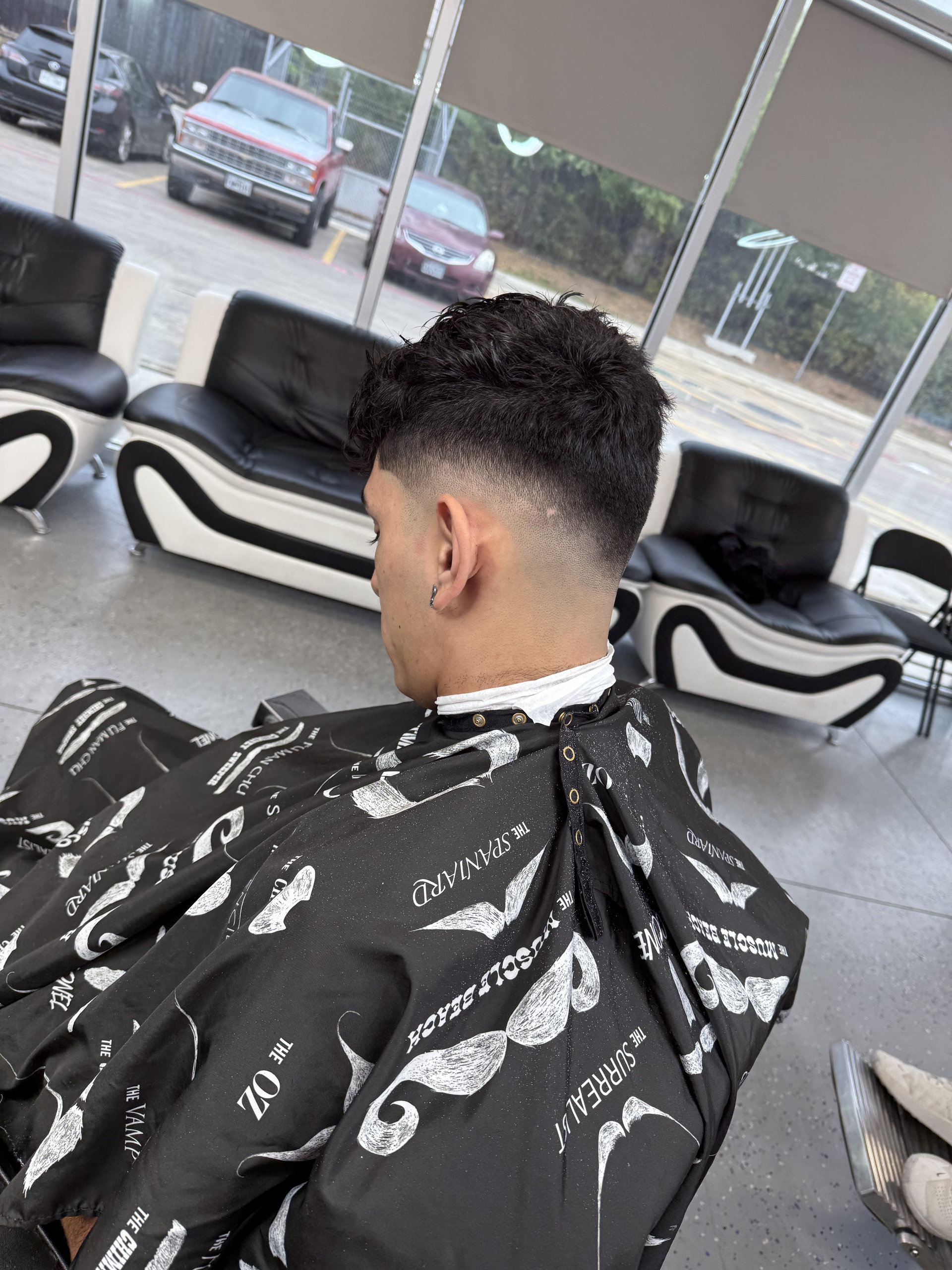 A person sits in a barber's chair wearing a patterned cape, showcasing a fresh, close-cropped fade haircut.