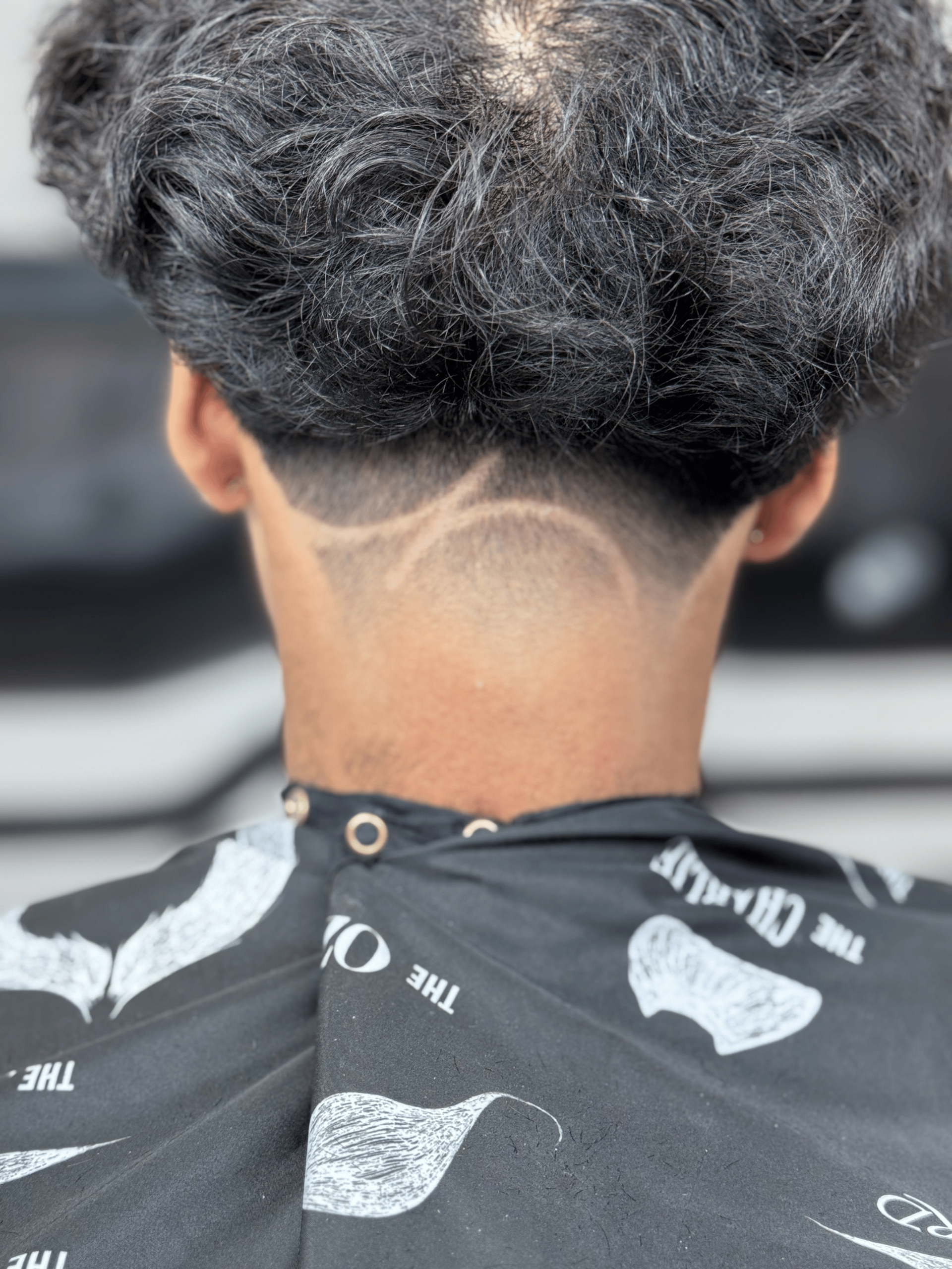 A close-up of a nape fade haircut featuring two curved shaved lines cut into the hair at the back of the neck.