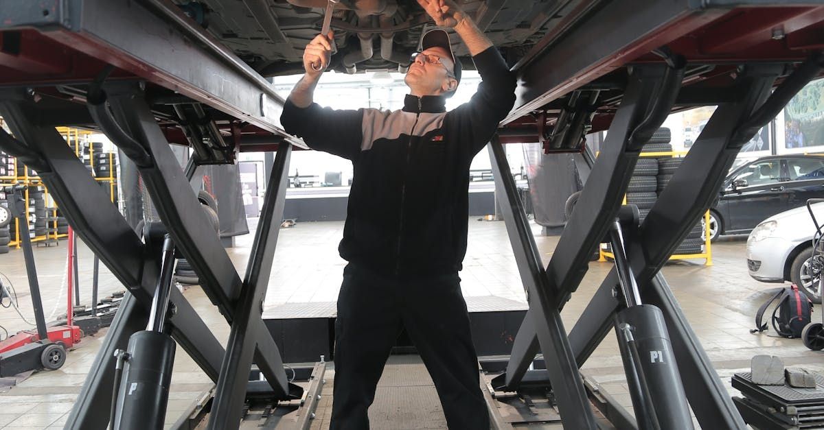 A man is working under a car on a lift in a garage. | All In One Auto