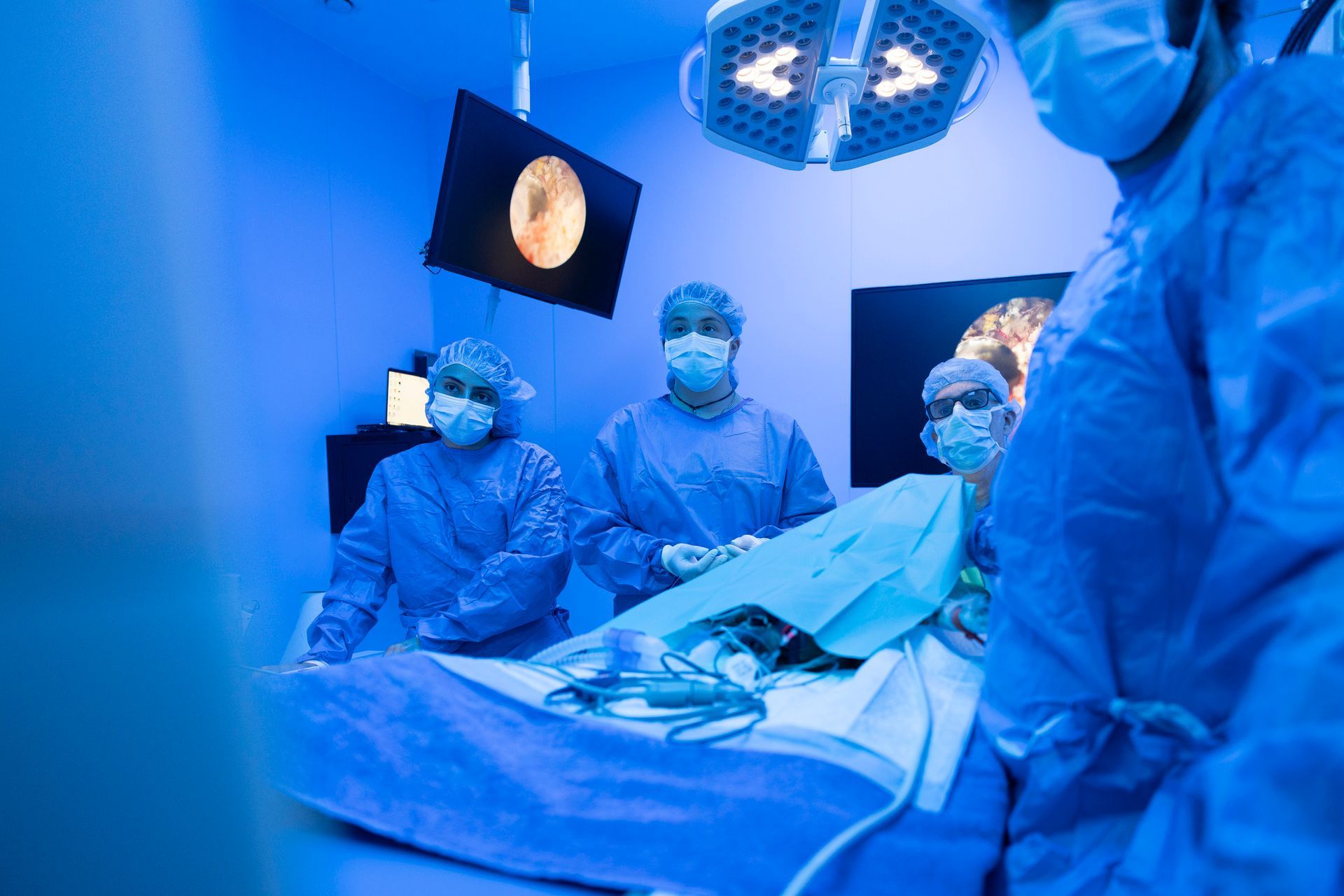 Equipe medica in sala operatoria, mentre esegue un intervento chirurgico sotto luci blu intense.