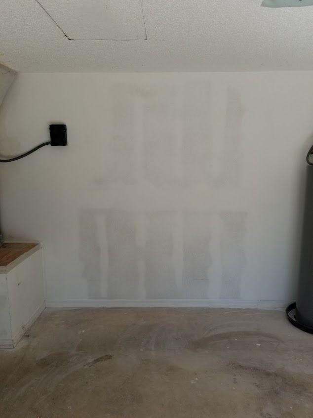 White wall in a garage with patches of filler, a black power box, and a concrete floor