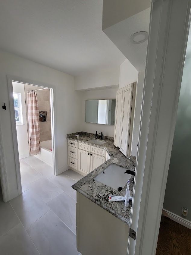 Bathroom with white cabinets, gray countertop, shower, and a doorway to a bedroom