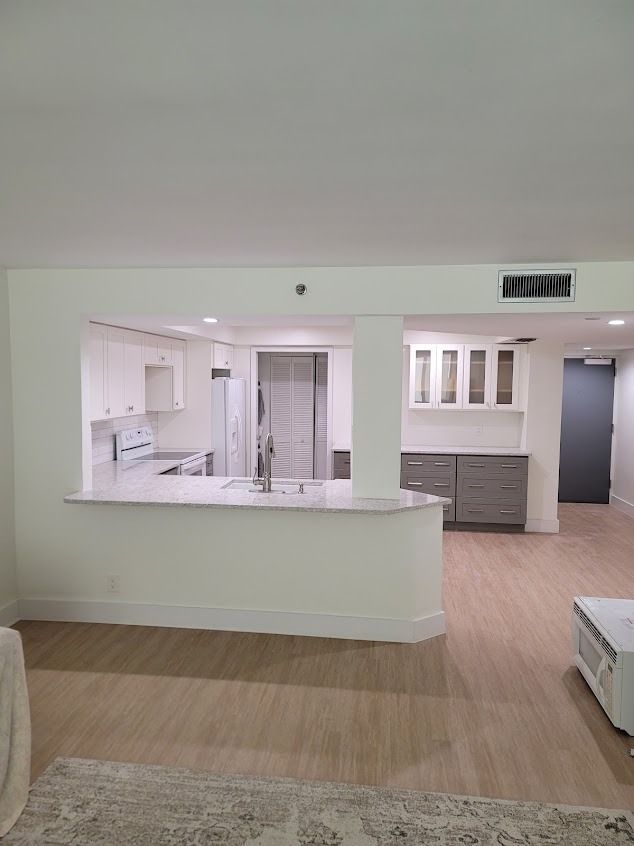 A remodeled kitchen open to a living area with white and gray cabinets, light wood floors