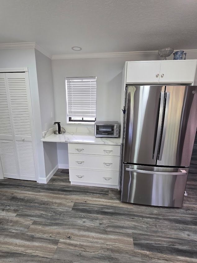 Kitchen with white cabinets, stainless steel refrigerator, and gray-wood flooring