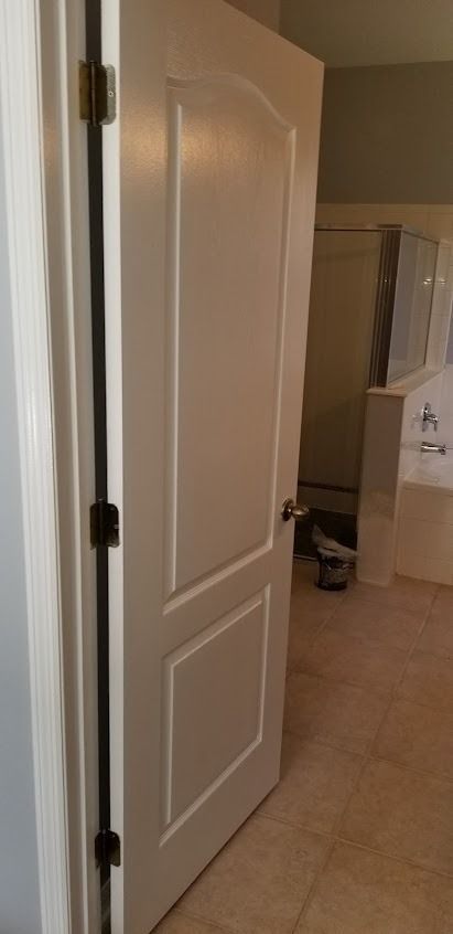 A white door with dark hinges, opening to reveal a bathroom with a tub and shower