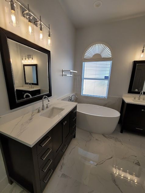Spacious modern bathroom with dark wood vanities, marble-look floors, and a standalone tub under arched window