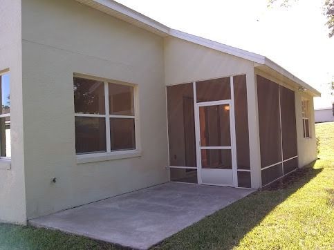 Exterior view of a light green house with a screened porch and concrete patio