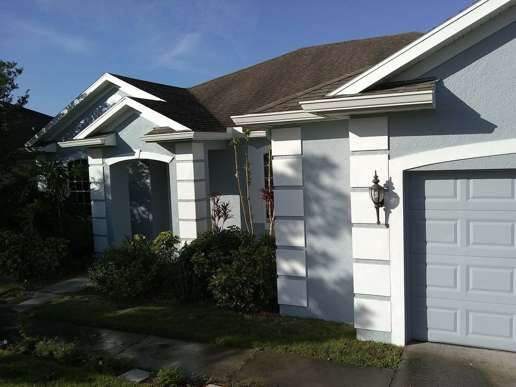Light blue house with white trim, brown roof, and a garage door