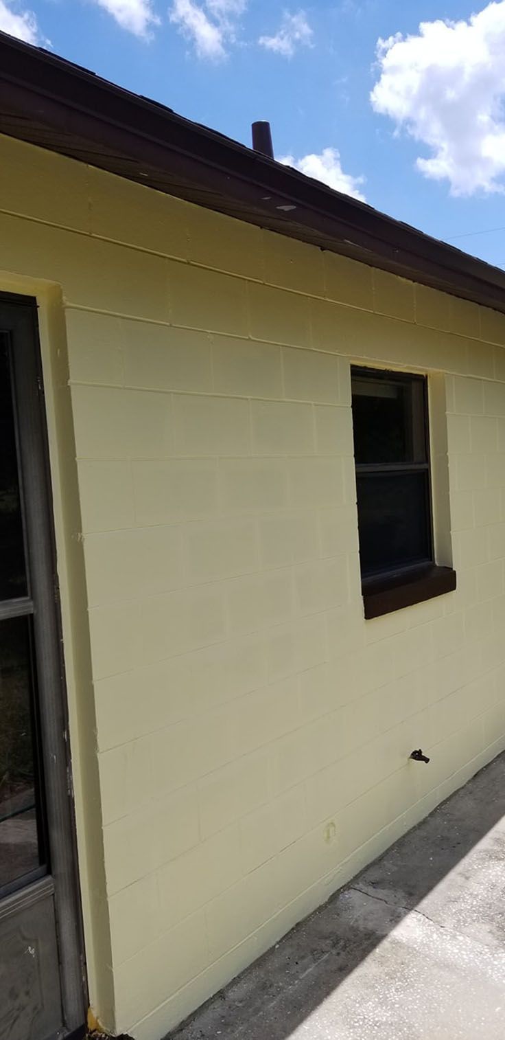 Exterior wall of a building, yellow paint, brown trim, window, dark gutter, partly cloudy sky