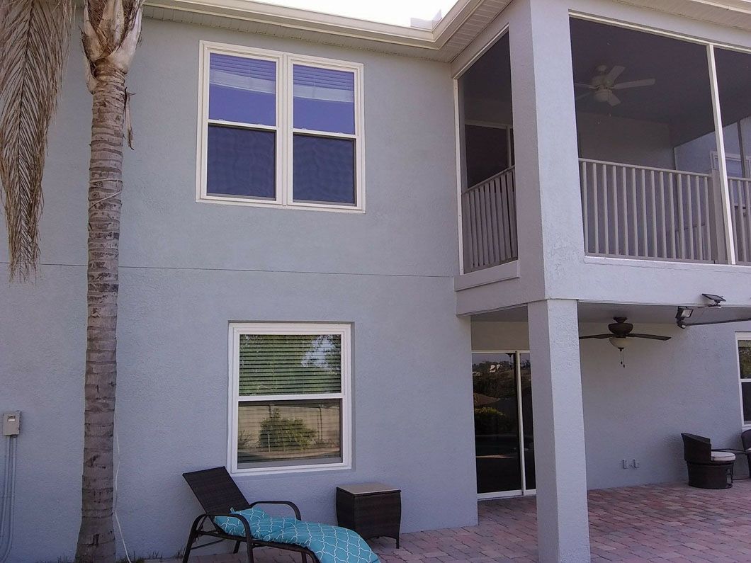 Two-story light blue house with white-framed windows, a screened-in porch, and a palm tree