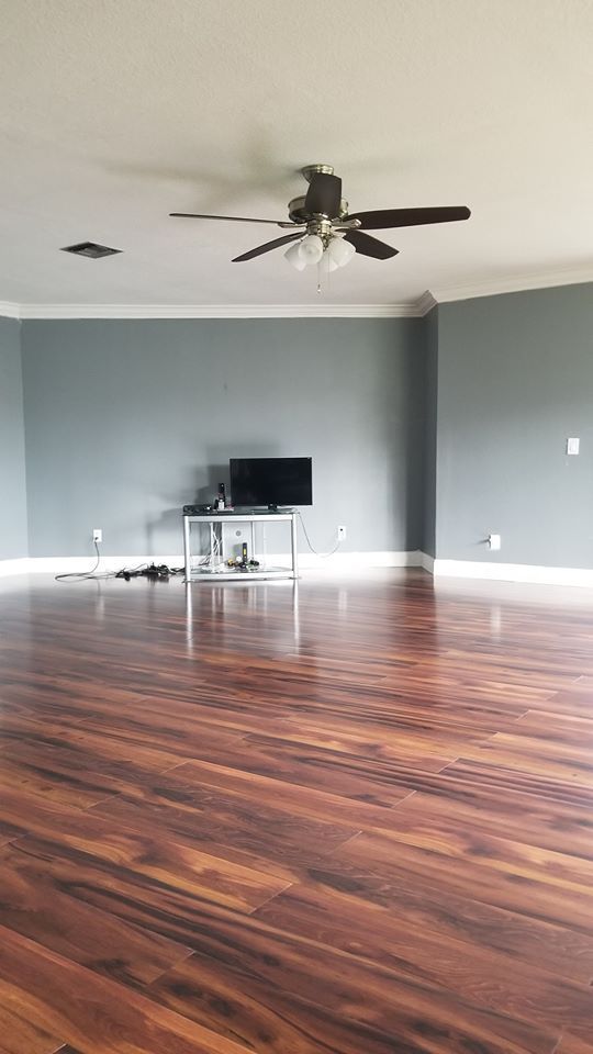 Empty living room with hardwood floors, gray walls, a TV on a stand, and a ceiling fan
