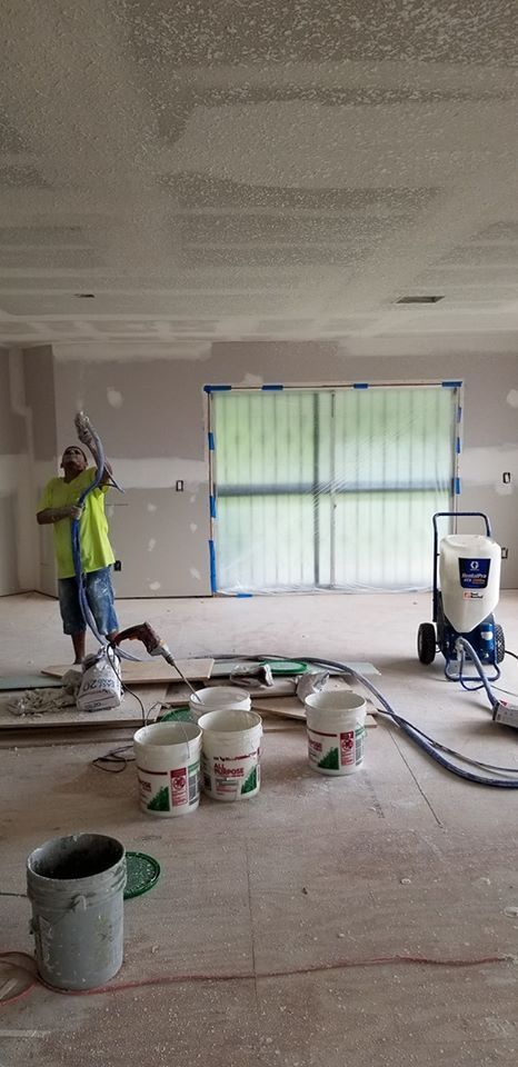 Person applying texture to a ceiling in a room with several paint buckets and a machine