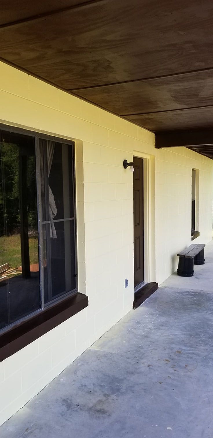 Exterior of a building with a porch, light walls, dark brown trim, and a bench