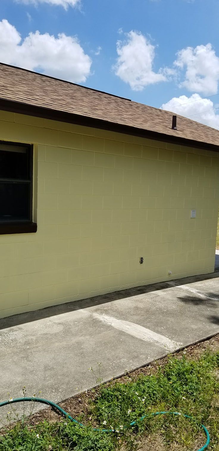 A yellow house with a brown roof and a concrete walkway under a blue sky