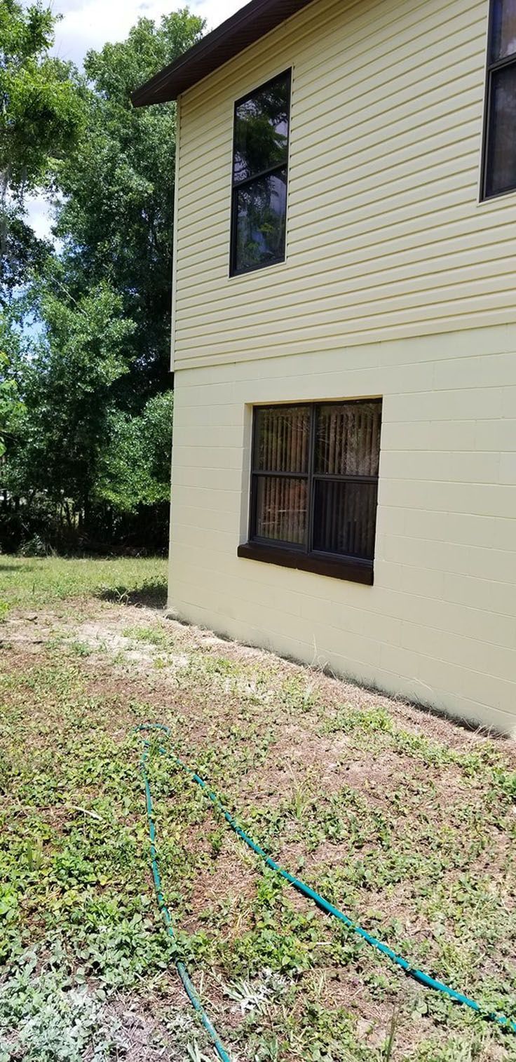 Exterior of a two-story building with beige siding and windows, in a grassy area with a green hose
