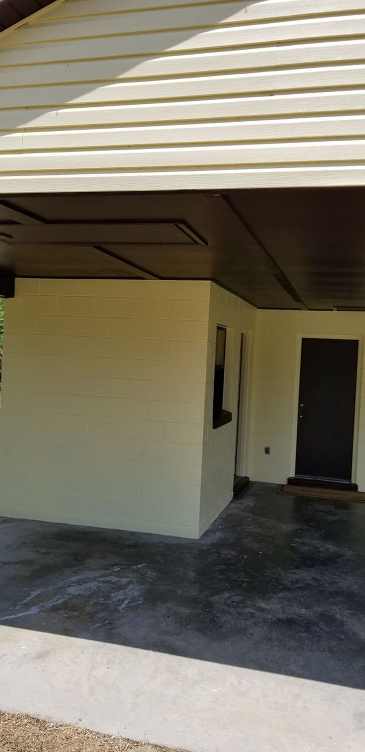 Exterior of a beige building with brown trim and a dark door, with a concrete floor