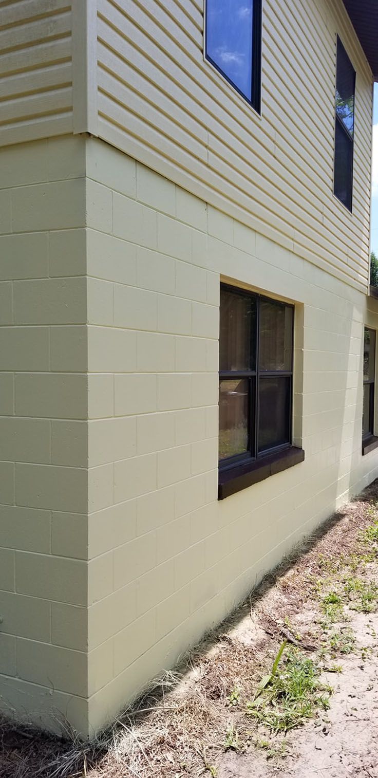 Corner of a two-story building with painted block walls, a window, and siding