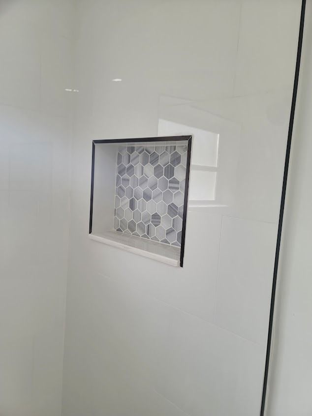 Built-in shower niche with mosaic tile, surrounded by white tiles and a black trim