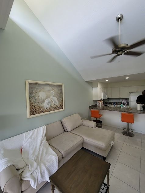 Living room with a white sectional sofa, small table, and bar with orange stools