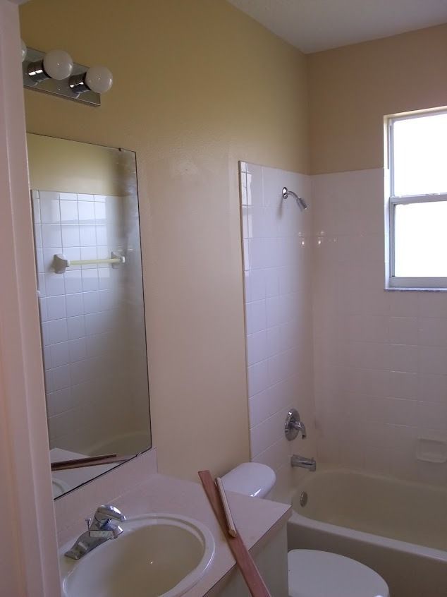 Bathroom with beige walls, white toilet and tub, sink, mirror, and small window.