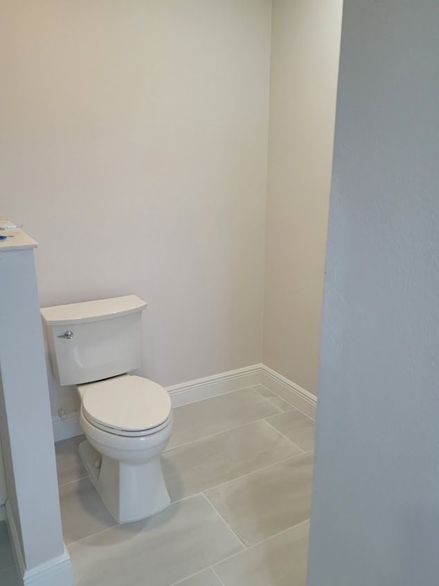 A white toilet in a small bathroom with gray tile floor and pale gray walls