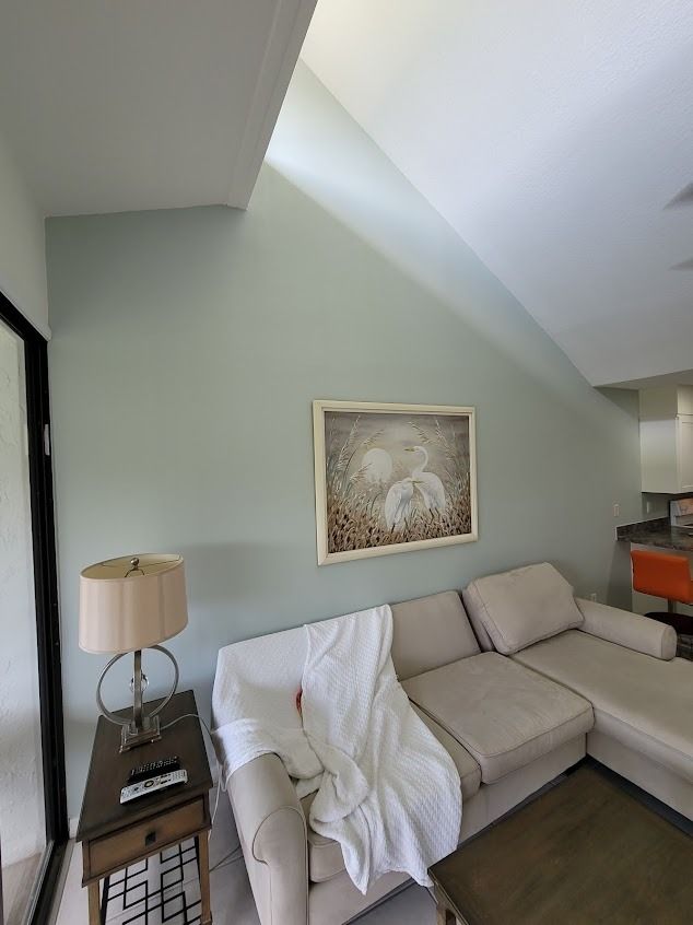 Living room with light green walls, beige sectional, artwork, and side table with lamp.