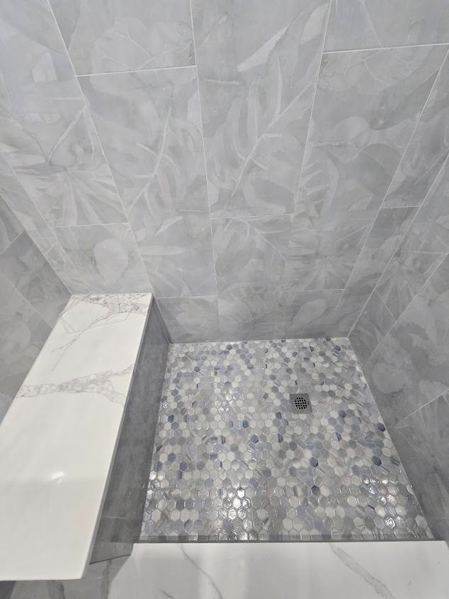 Gray and white tiled shower with built-in bench and mosaic floor