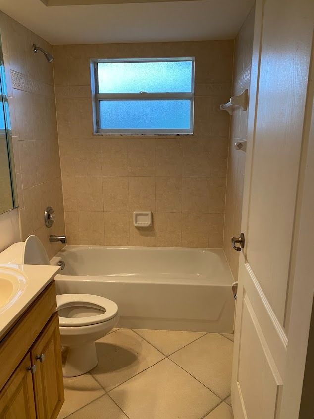 Bathroom with a white tub, toilet, and tan tile walls. Window above the tub